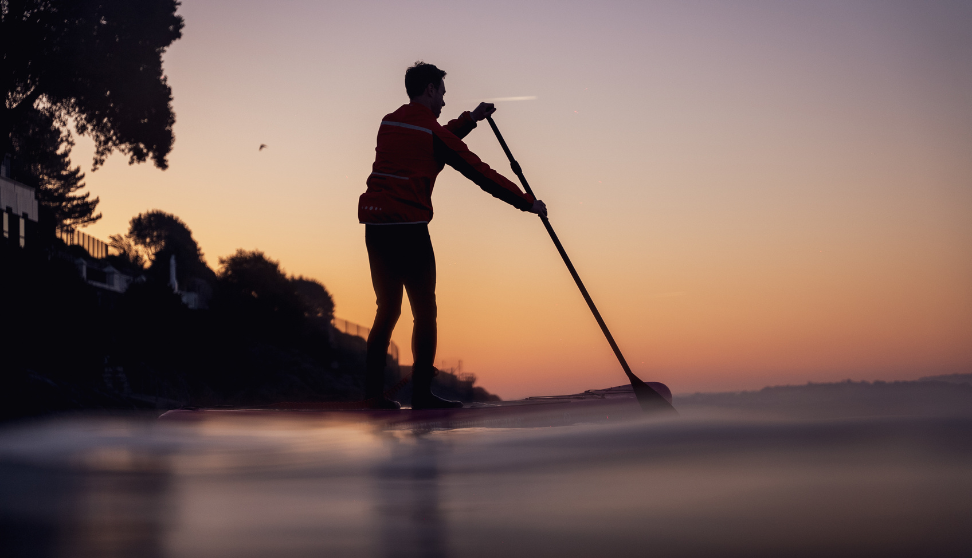 Silhouette of a person paddleboarding on calm water at sunset.